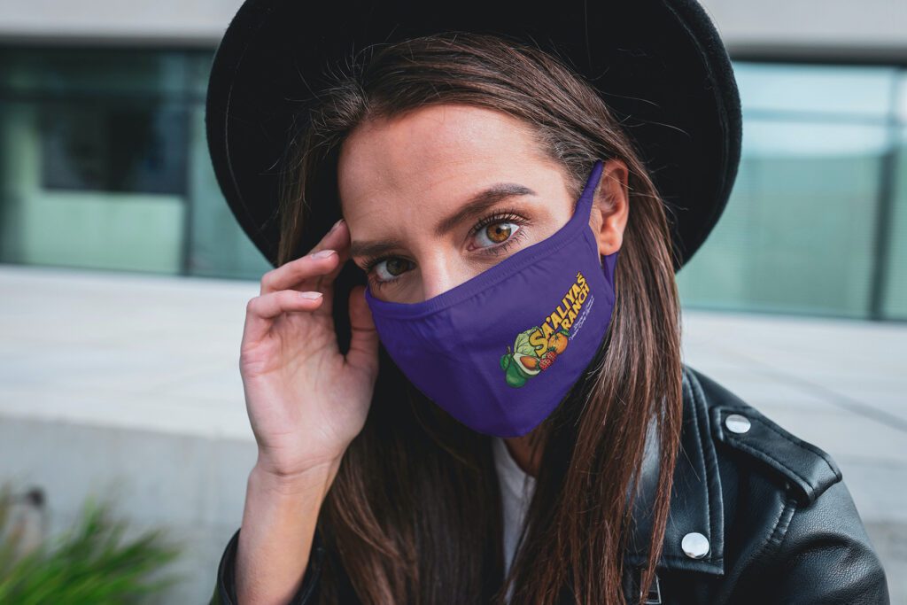 Rendering: A woman with long brown hair models a purple Sa-Aliyaš Ranch cloth facemask