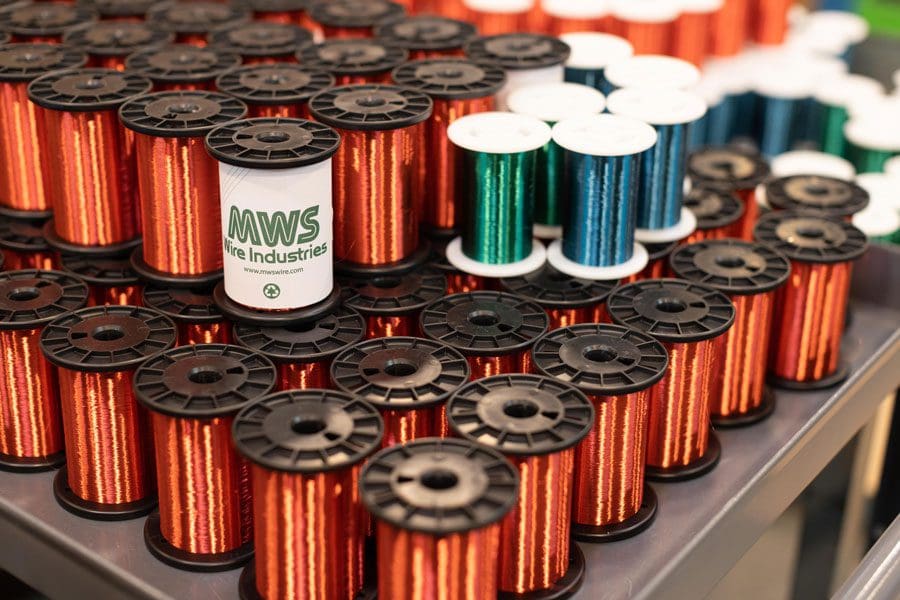 Manufacturing video and photography image of several spools of colored wire, mainly red and some green and blue, are displayed on a table. In the photo, a central spool bears the label "MWS Wire Industries."