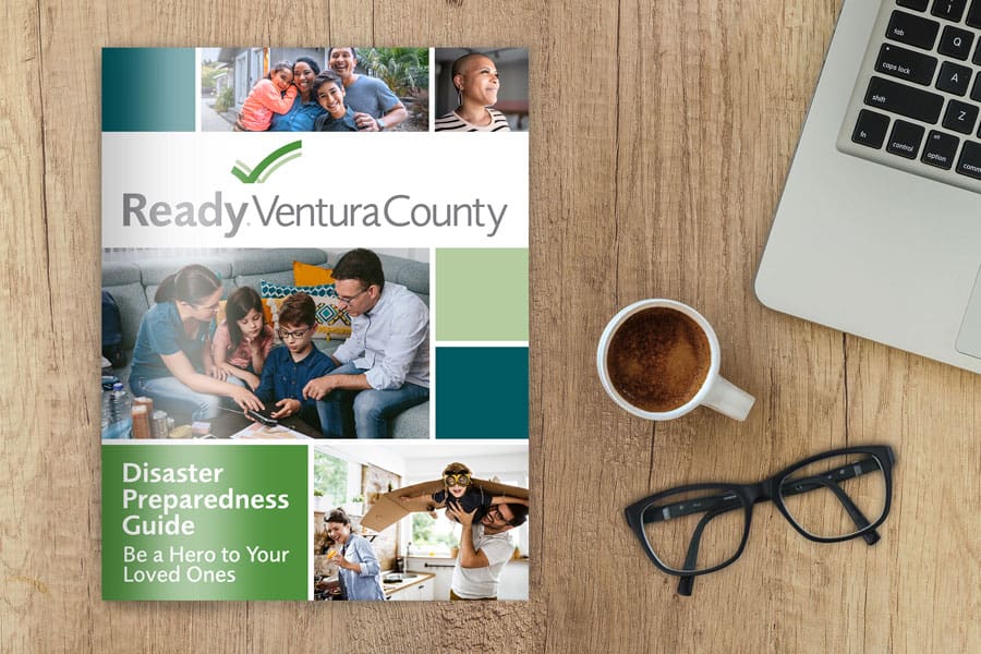 VCPreparednessGuide_00v2 A "Ready Ventura County" brochure sits on a wooden table beside a laptop, eyeglasses, and a cup of coffee.