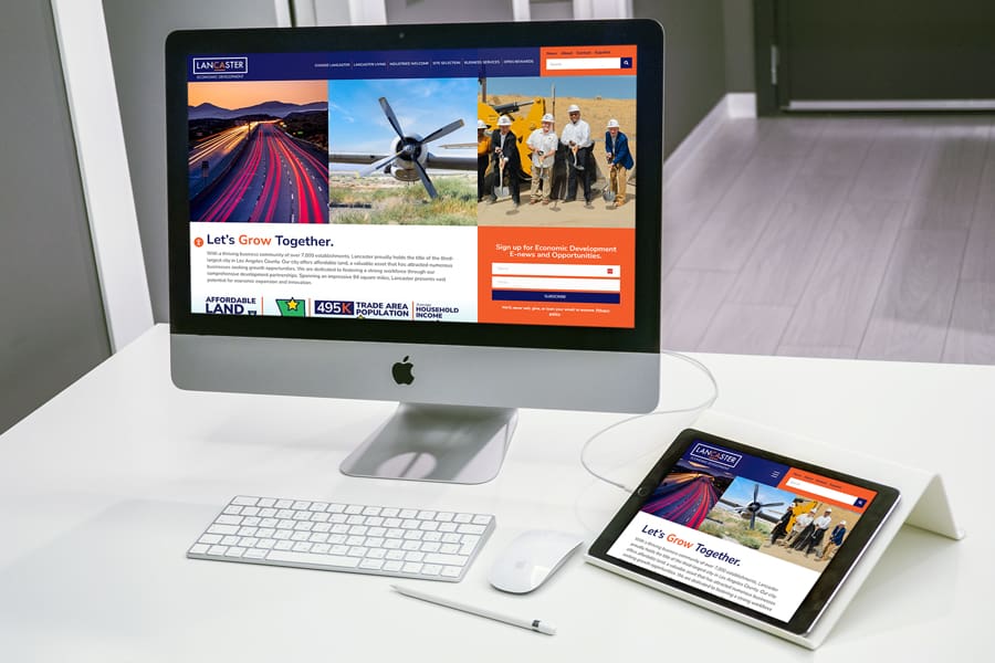 A computer and tablet on a desk display a website with images of landscapes and a plane. Text on the site includes Lets Grow Together and highlights Lancaster Economic Development as a catalyst for regional growth.