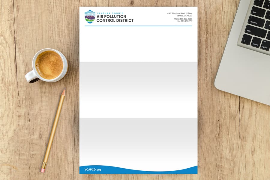 VCAPCD_Portfolio_03 A cup of coffee, pencil, and a letterhead featuring the logo and branding of Ventura County Air Pollution Control rest on a wooden desk.