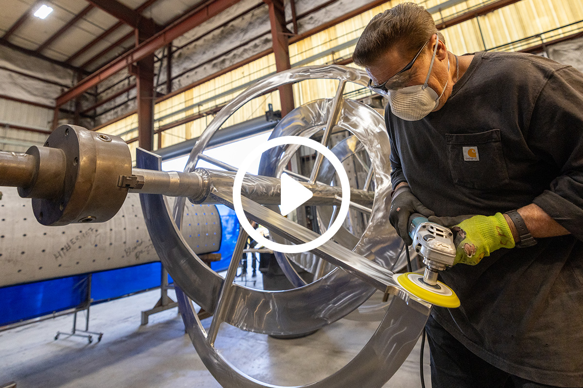 Worker polishing metal sculpture in industrial workshop with safety gear.